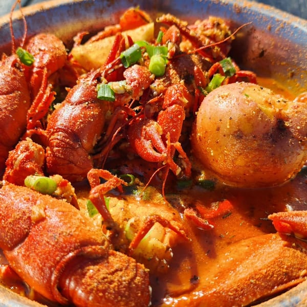 Boiled crawfish, potatoes, and corn in a spicy broth, garnished with green onions.