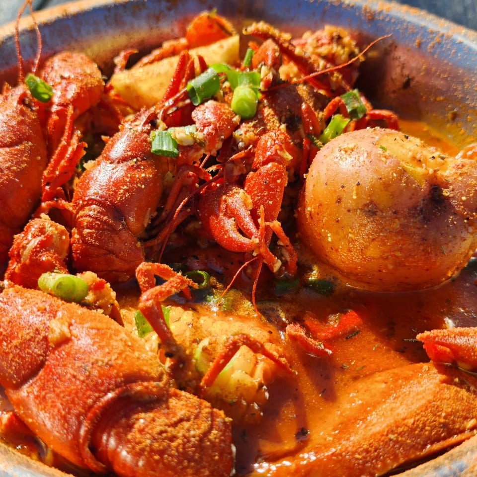 Boiled crawfish, potatoes, and corn in a spicy broth, garnished with green onions.