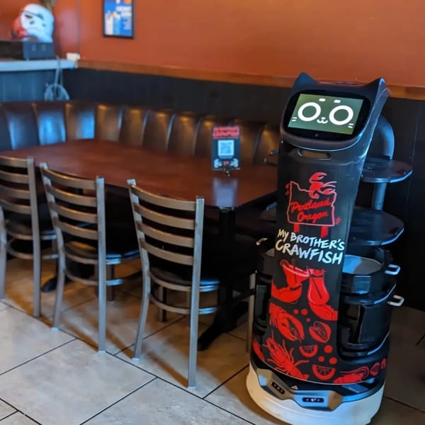 A cat-faced robot with "My Brother's Crawfish" branding stands next to a dining table.