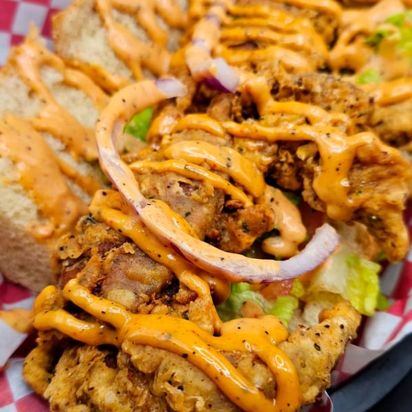 Close-up of a My Brother's Crawfish po'boy, featuring fried seafood, sauce, lettuce, and onions.