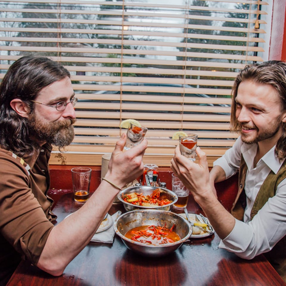 Two men toasting with shots at a table with bowls of crawfish at My Brother's Crawfish.