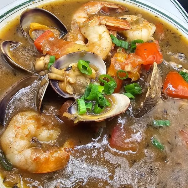 Close-up of My Brother's Crawfish seafood gumbo with shrimp, clams, tomatoes, and green onions.