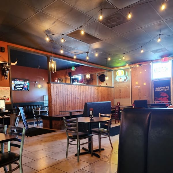 Interior of My Brother's Crawfish restaurant with tables, booths, string lights, and a TV.