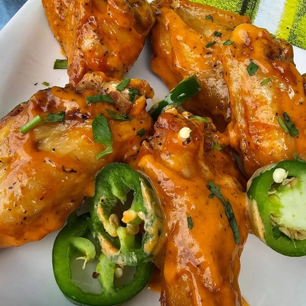 Spicy orange chicken wings with green jalapeño slices on a white plate.