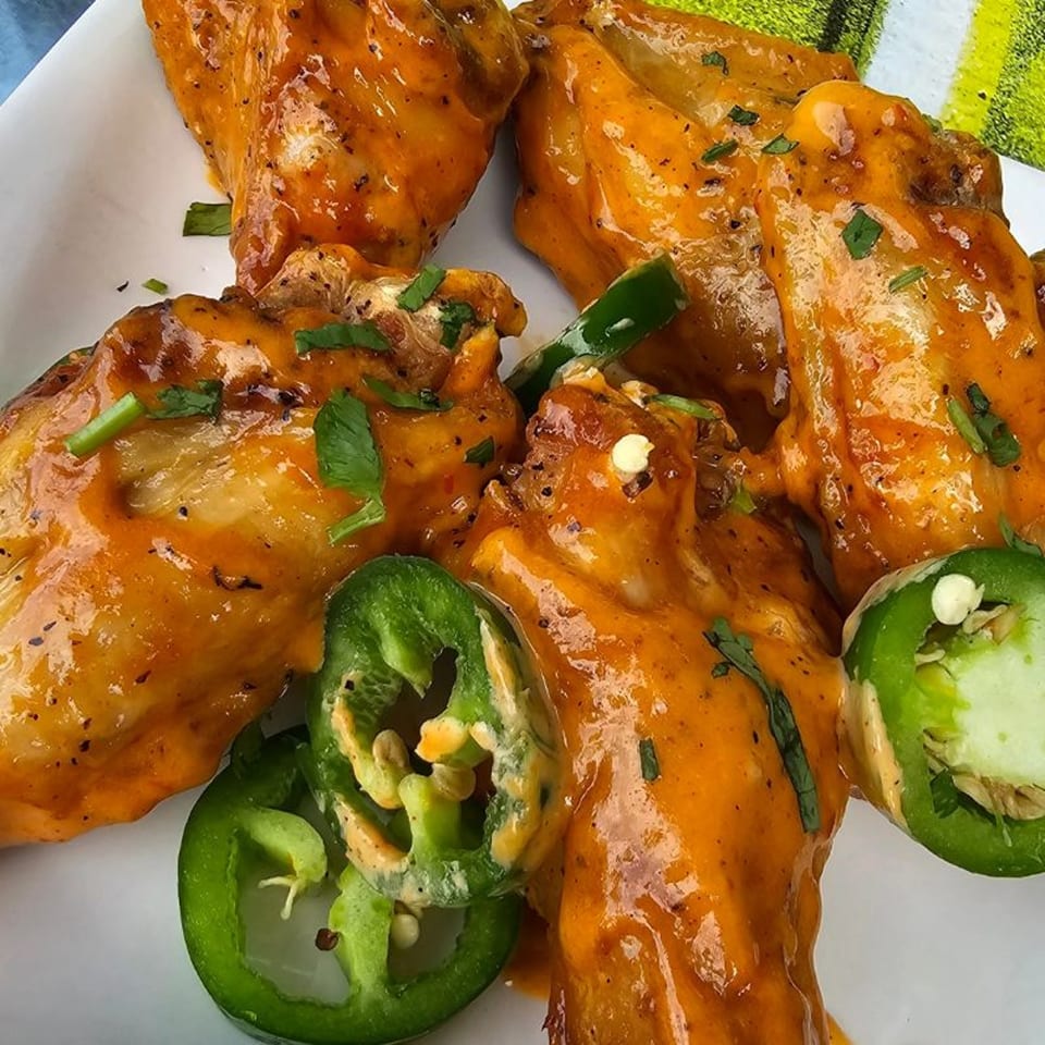 Spicy orange chicken wings with green jalapeño slices on a white plate.