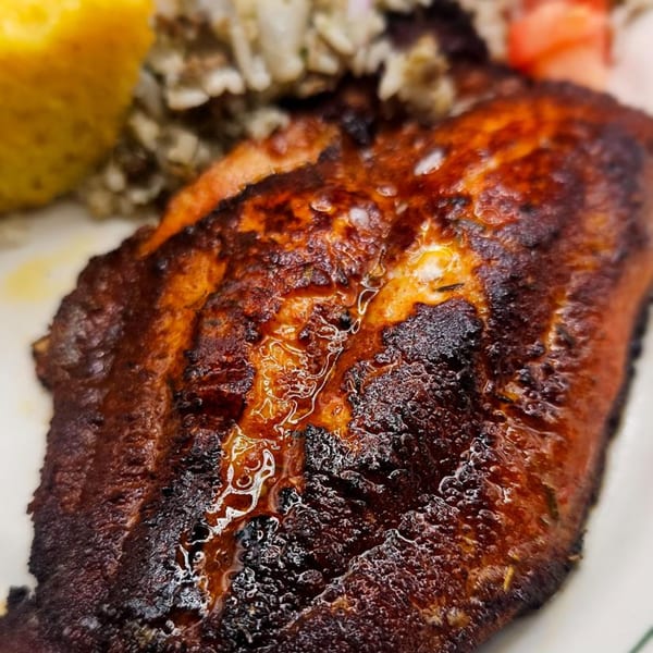 Close-up of a perfectly seared, blackened fish fillet with a side of rice and lemon.