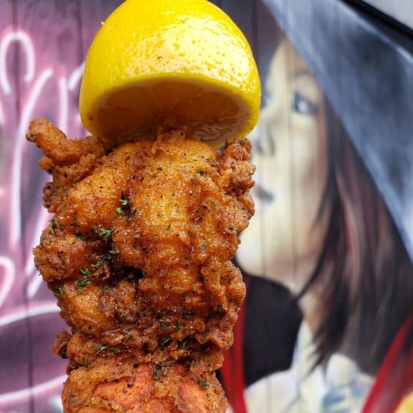 Crispy fried seafood, possibly crawfish, with a lemon half on top, against a blurred mural.