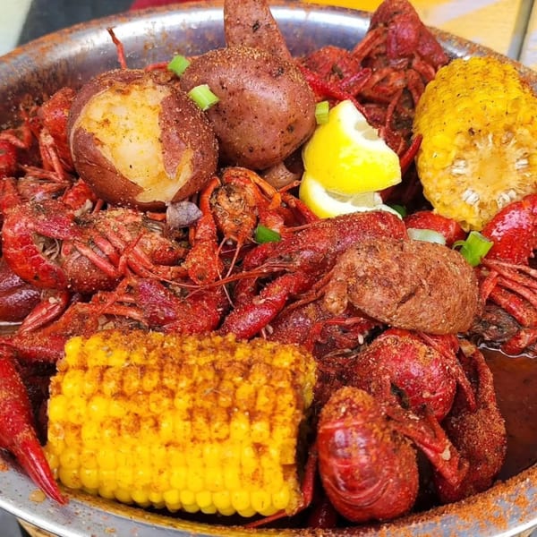 A metal bowl filled with My Brother's Crawfish seafood boil, including red crawfish, corn, potatoes, and lemon.